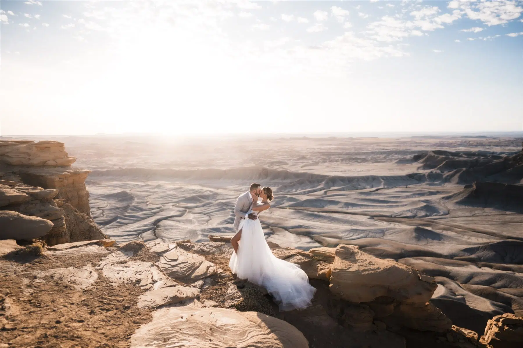 Couple doing a dip kiss in wedding clothes on their elopement in utah standing on the edge of a cliff with a desert landscape behind them