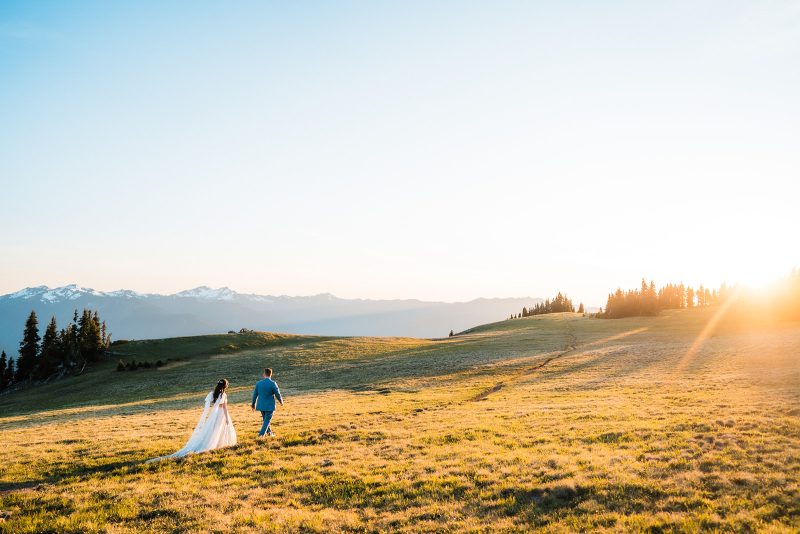 Wedding couple hiking through a grassy meadow in the mountains at sunset